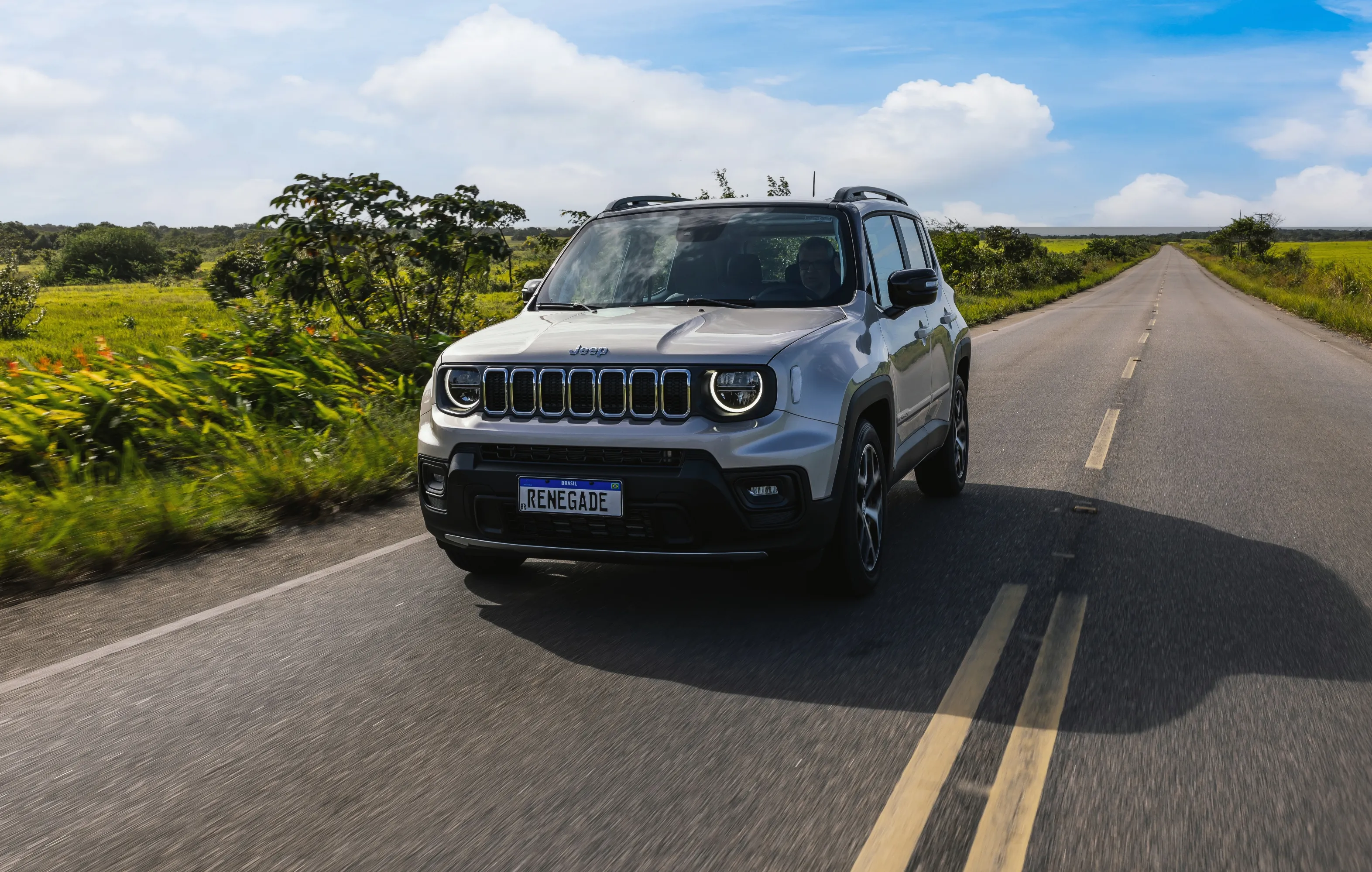 Vista frontal de Jeep Renegade na cor cinza em estrada com vegetação baixa e média na lateral