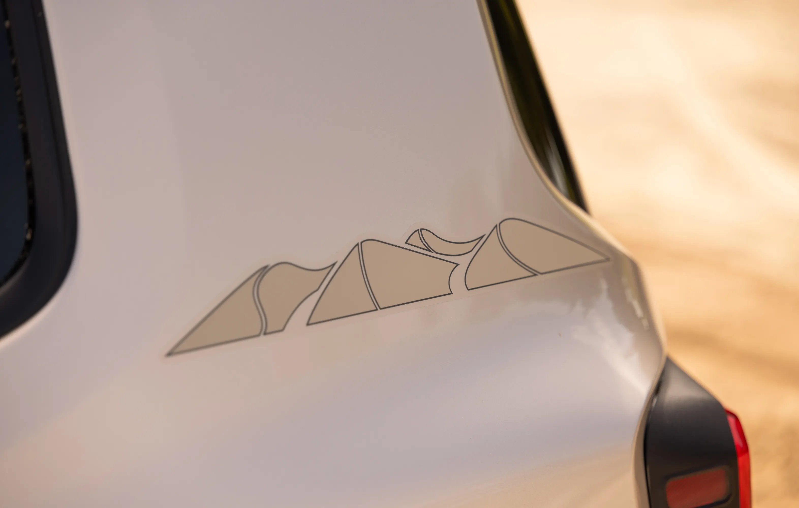 Detalhe da coluna traseira do Jeep Renegade com adesivo exclusivo da versão Sahara, com formas triangulares de pontas arredondadas fazendo referência às dunas do Deserto do Saara.