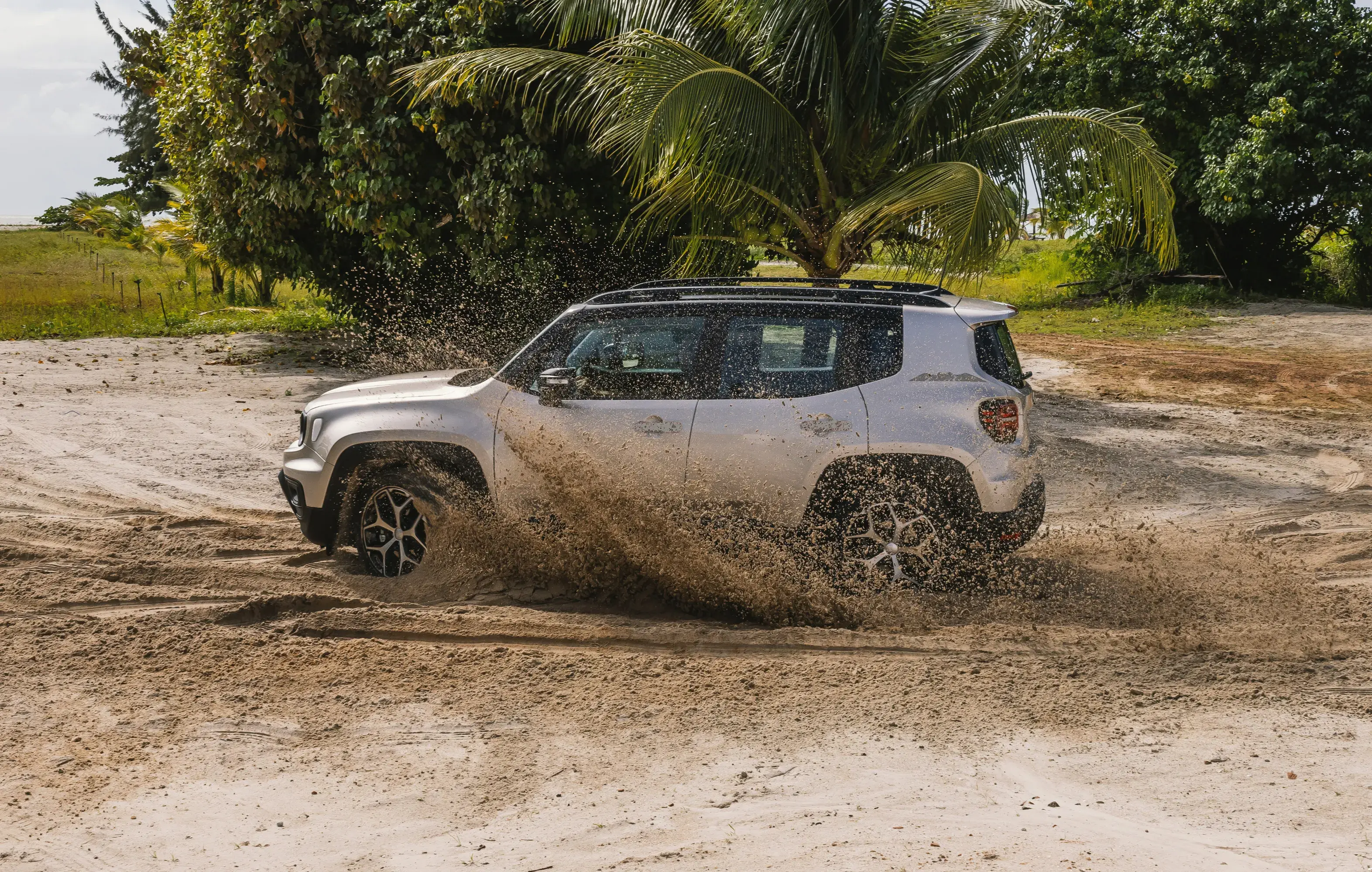 Vista lateral de Jeep Renegade na cor prata passando em alta velocidade por terreno arenoso, levantando areia durante movimento