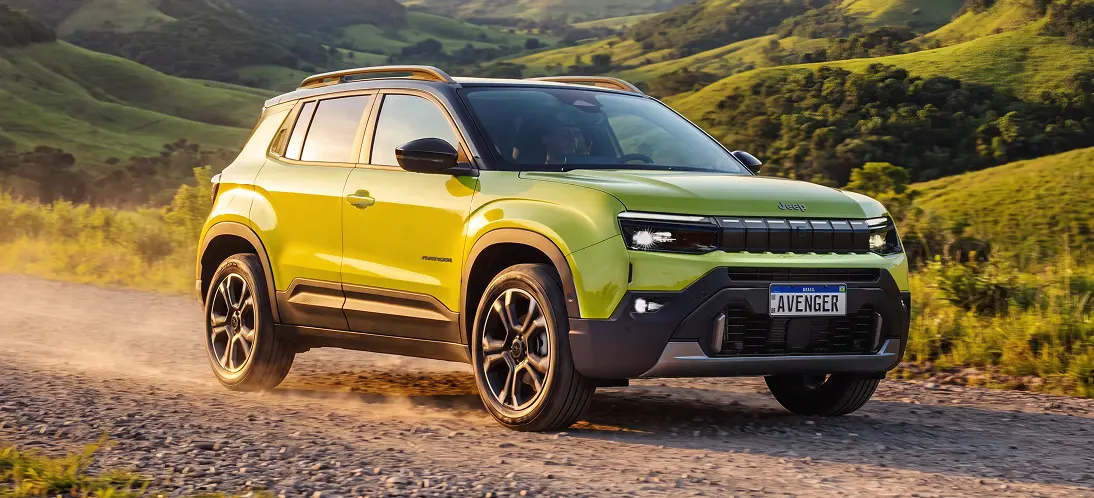 Altura livre do solo de 221 mm Jeep Avenger verde com parte frontal e lateral visíveis, rodas de liga leve e carroceria elevada em estrada de terra entre montanhas.