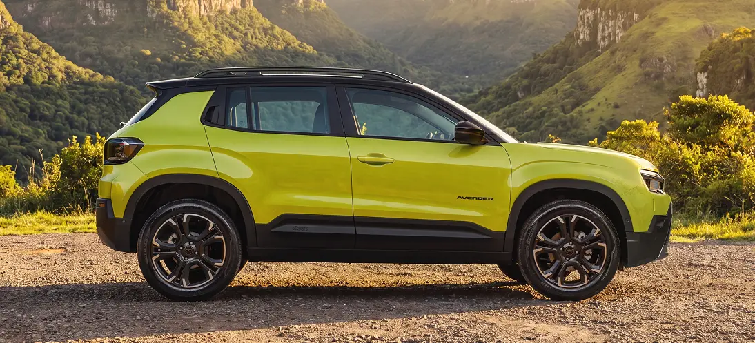 Dimensões para qualquer rotina Jeep Avenger verde com lateral completa visível, rodas de liga leve e teto preto, estacionado em terreno de pedras com montanhas ao fundo.
