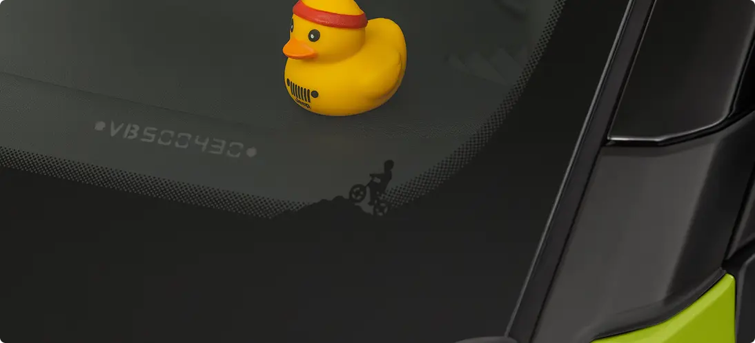 Legado em cada detalhe Patinho amarelo de borracha com logotipo Jeep posicionado sobre vidro traseiro do Jeep Avenger, com ilustração de ciclista visível no acabamento ao fundo.