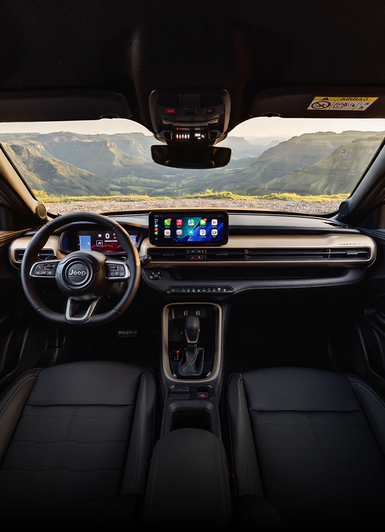 Interior do Jeep Avenger com volante multifuncional, painel digital, central multimídia, console central e montanhas visíveis pelo para-brisa.