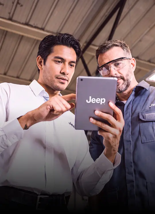 Duas pessoas observam tablet com logotipo Jeep em ambiente interno com estrutura metálica ao fundo.