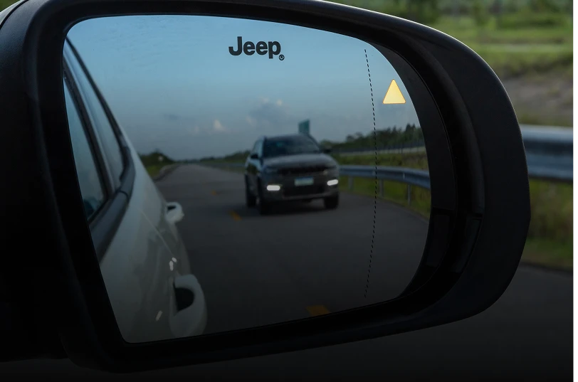 Retrovisor lateral do Jeep Commander exibindo alerta de ponto cego, com outro veículo se aproximando pela pista.