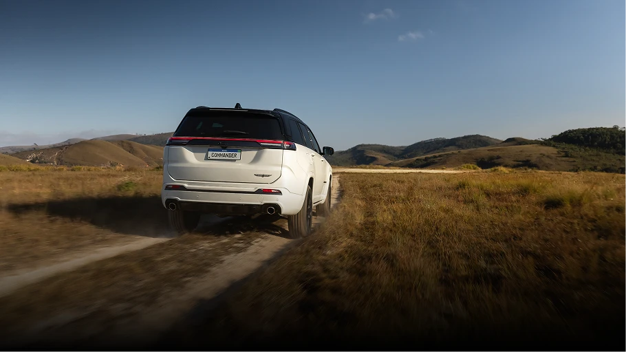 Traseira do Jeep Commander branco estacionado em área de campo aberta com vegetação seca.