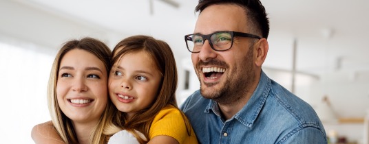 Homem, mulher e criança olhando para frente e sorrindo